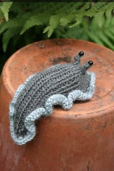 a small crocheted lizard sitting on top of a brown object next to some plants