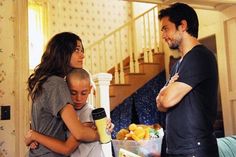 a man and woman standing next to each other in a living room with food on the table