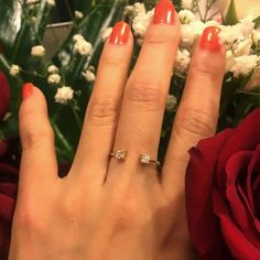 a close up of a person's hand with a ring on it and flowers in the background