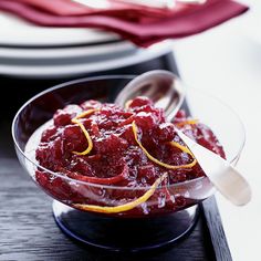 a bowl filled with cranberry sauce on top of a wooden table next to plates