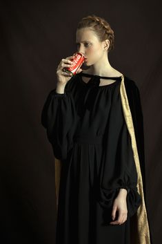 a woman in a black dress drinking from a red can with gold trim around her neck