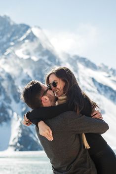 a man and woman hugging each other in front of snow covered mountains