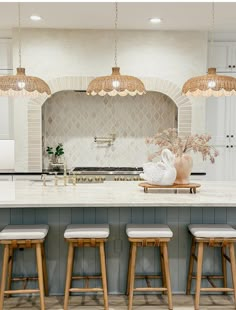 a kitchen with four stools in front of an island and several lights above it