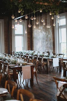 the tables are set up for an event with hanging chandeliers and greenery