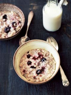 two bowls filled with oatmeal next to a bottle of milk and spoons