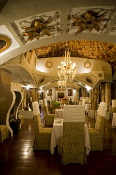 a dining room with tables and chairs covered in white tablecloths, chandeliers and ceiling decorations