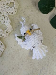 a crocheted white bird ornament sitting on top of a table next to green leaves