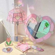 a pink heart shaped mirror sitting on top of a wooden table next to a lamp