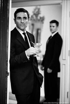 a man in a suit and tie holding a glass with another man standing behind him