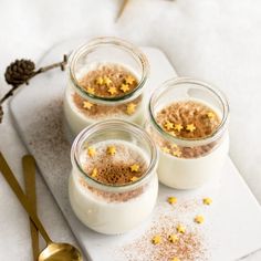 three small glass jars filled with food on top of a white tray next to gold spoons