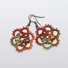 two pairs of colorful earrings on a white surface, one with an intricate design and the other with beads