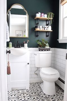 a white toilet sitting under a bathroom mirror next to a sink and a wooden shelf