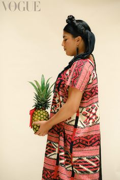 a woman holding a pineapple in her hand and wearing a dress with an ethnic pattern