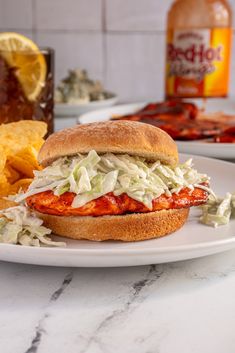 a chicken sandwich with coleslaw and chips on a plate next to a bottle of booze