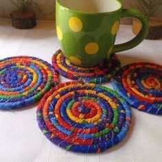 four colorful coasters on a table next to a coffee cup and pot holder with polka dots