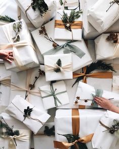 many wrapped presents are stacked on top of each other with ribbons and pine cones tied to them