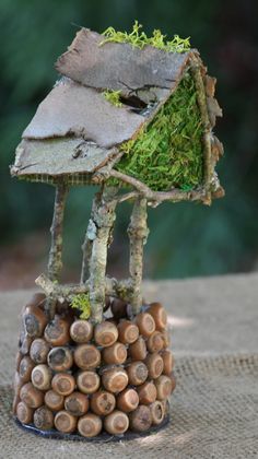 a small house made out of wood and moss on top of some rocks with trees in the background