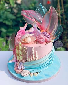 a multi layer cake decorated with pink and blue frosting, seashells and flowers