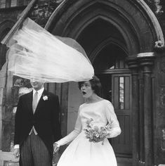 a bride and groom walking out of an old church holding their veil over their heads