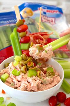 a white bowl filled with dip surrounded by celery, tomatoes and olives