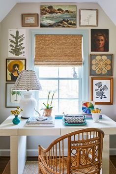 a white desk topped with a lamp next to a window covered in pictures and paintings