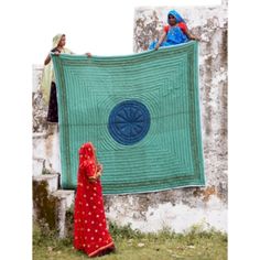 two women standing next to each other holding up a large blue quilt on a wall