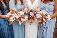 three bridesmaids in blue dresses holding bouquets of flowers and feathers on their arms