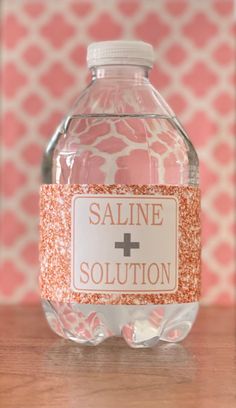 a bottle of saline solution sitting on top of a wooden table next to a pink and white wall