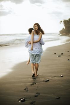 a man carrying a woman on his back as they walk along the beach with footprints in the sand