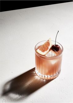 a drink with an orange slice and a cherry on the rim, sitting on a white surface