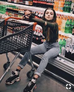 a woman sitting on top of a shopping cart in a grocery store with her legs crossed