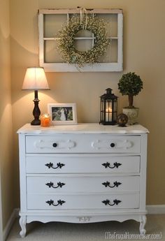 a white dresser sitting in a room next to a lamp and pictures on the wall