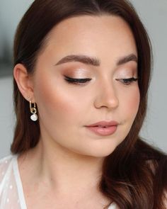 a woman with long brown hair wearing a white top and gold earrings, looking down at her face