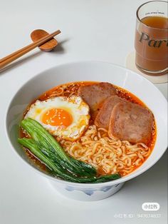 a bowl filled with noodles, meat and vegetables next to a cup of tea on a table