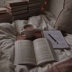 an open book and cup of coffee sit on a bed with books stacked in the background