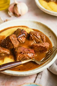 a white plate topped with meat and gravy covered in sauce next to garlic