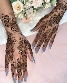 two hands with henna designs on them and flowers in the backgroung