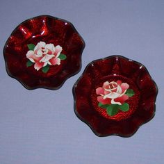 two red glass dishes with flowers painted on the side and one has a white rose