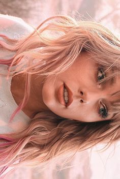 a woman with long blonde hair and blue eyes posing for a photo in front of a pink background