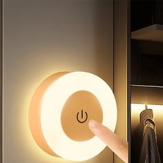 a person's hand is pressing the button on a wall light that has a circular shape