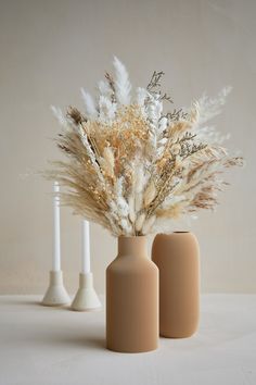 three vases with dried plants in them on a table