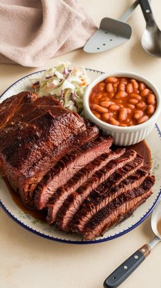 a plate topped with meat, beans and coleslaw next to a bowl of baked beans