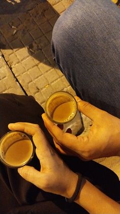 two hands holding cups of beer on the ground