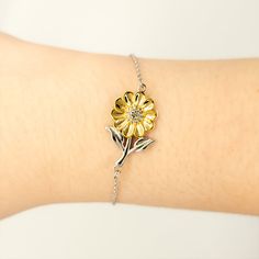 a woman's arm with a yellow flower bracelet on her left wrist and a white background