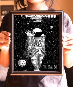 a woman holding up a framed poster with an astronaut on it