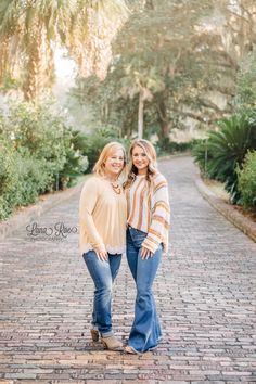 two women standing together on a brick path in front of palm trees and other greenery