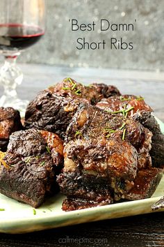 a white plate topped with short ribs next to a glass of wine