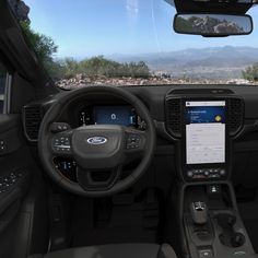 the interior of a vehicle with dashboard, steering wheel and touch screen monitor showing mountains in the distance