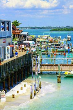 a pier with several boats docked at it and people walking on the beach near by