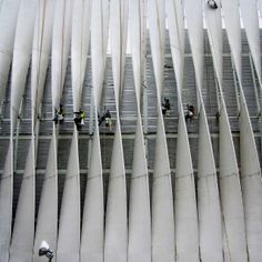 several skiers are skiing down the side of a tall building with vertical slats on it